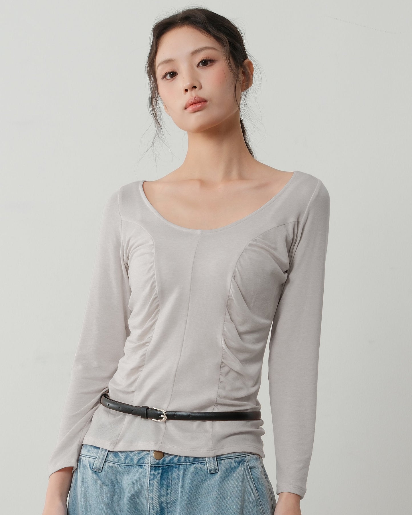 Woman wearing a light gray long-sleeve top and blue jeans on a plain background