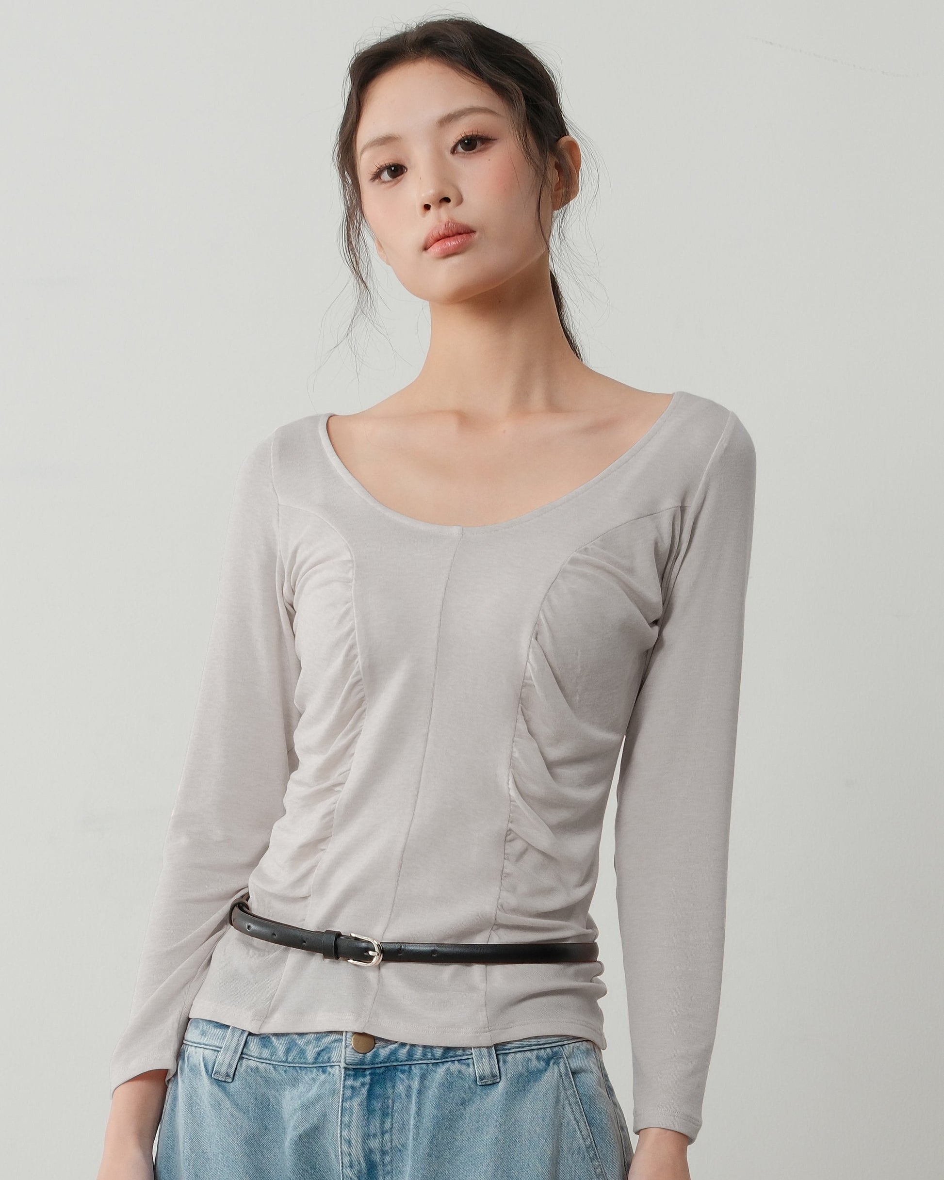 Woman wearing a light gray long-sleeve top and blue jeans on a plain background
