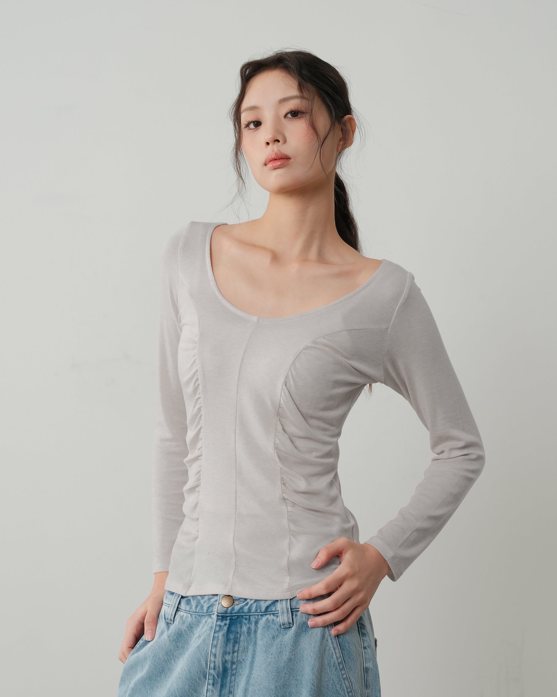 Woman wearing a light gray long-sleeve top and blue jeans against a plain background