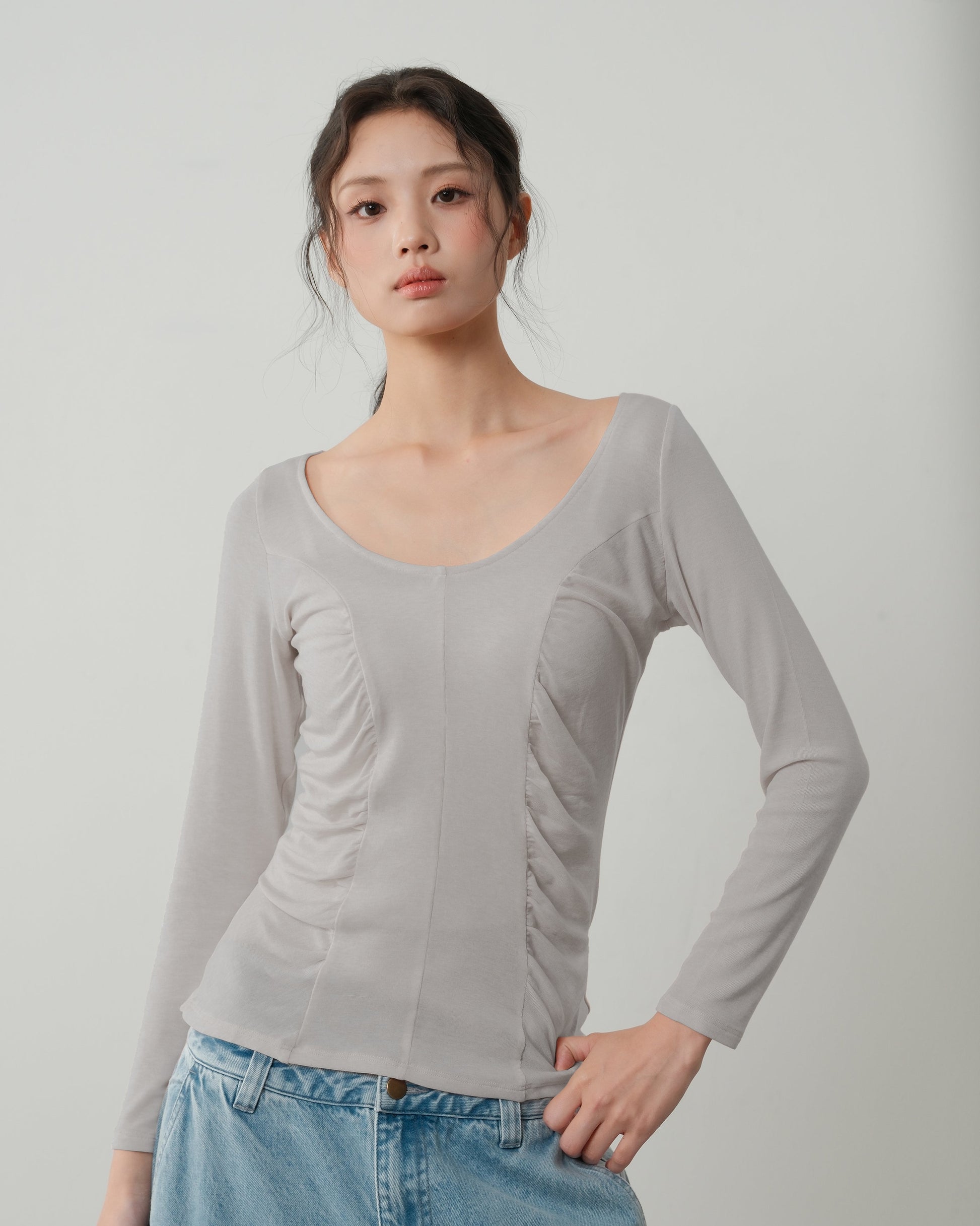 Woman wearing a light gray long-sleeve top and blue jeans against a plain background