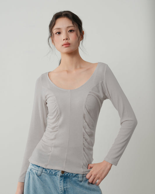 Woman wearing a light gray long-sleeve top and blue jeans against a plain background