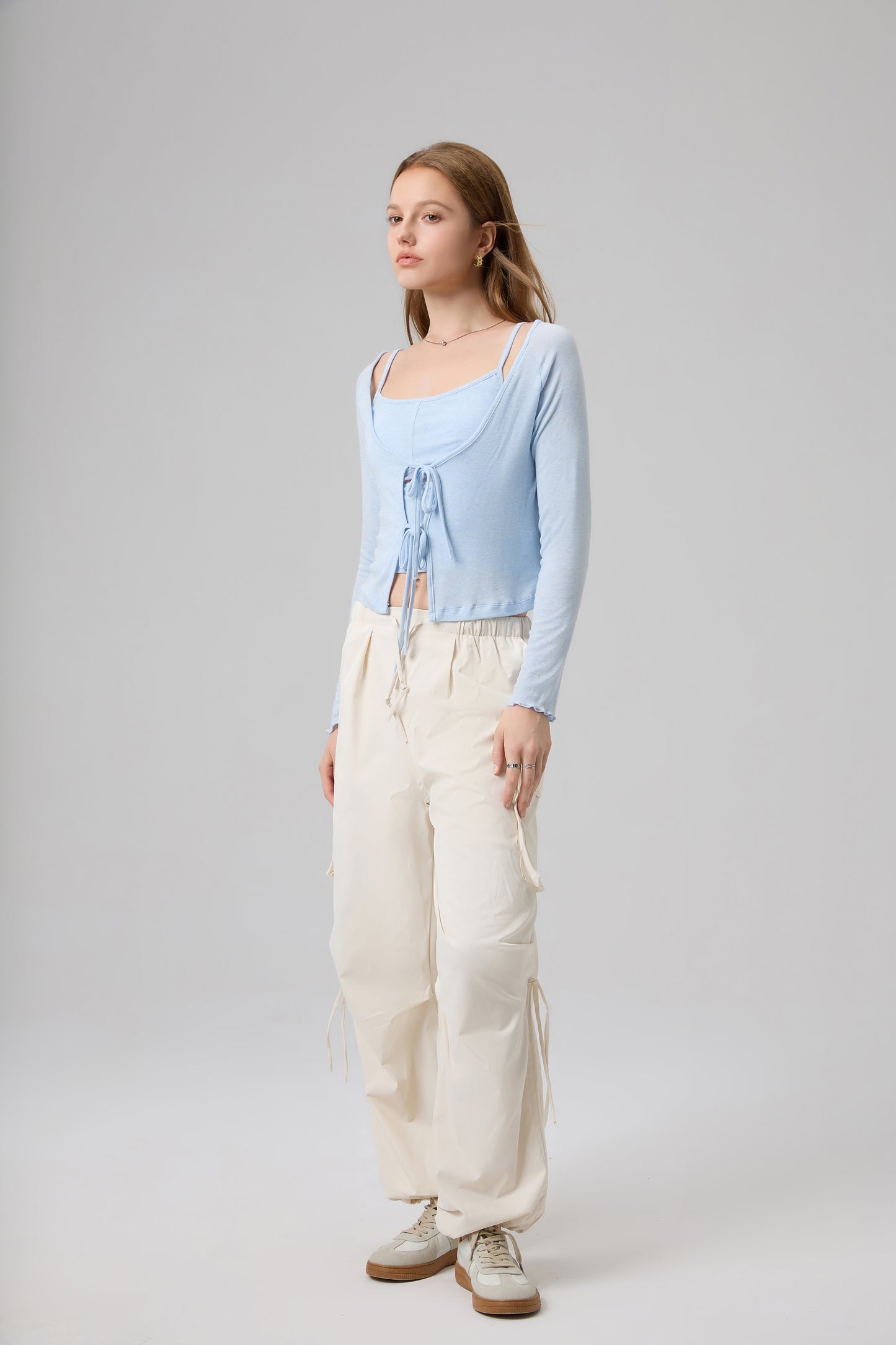 Woman wearing a light blue top and white pants on a gray background