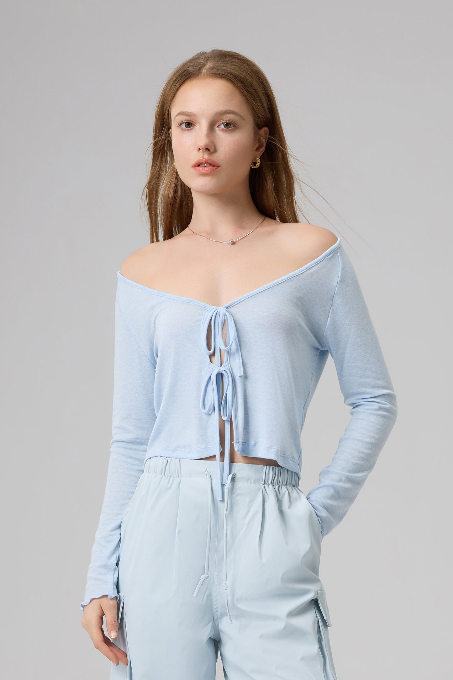 Woman wearing a light blue off-shoulder top and wide-leg pants on a gray background