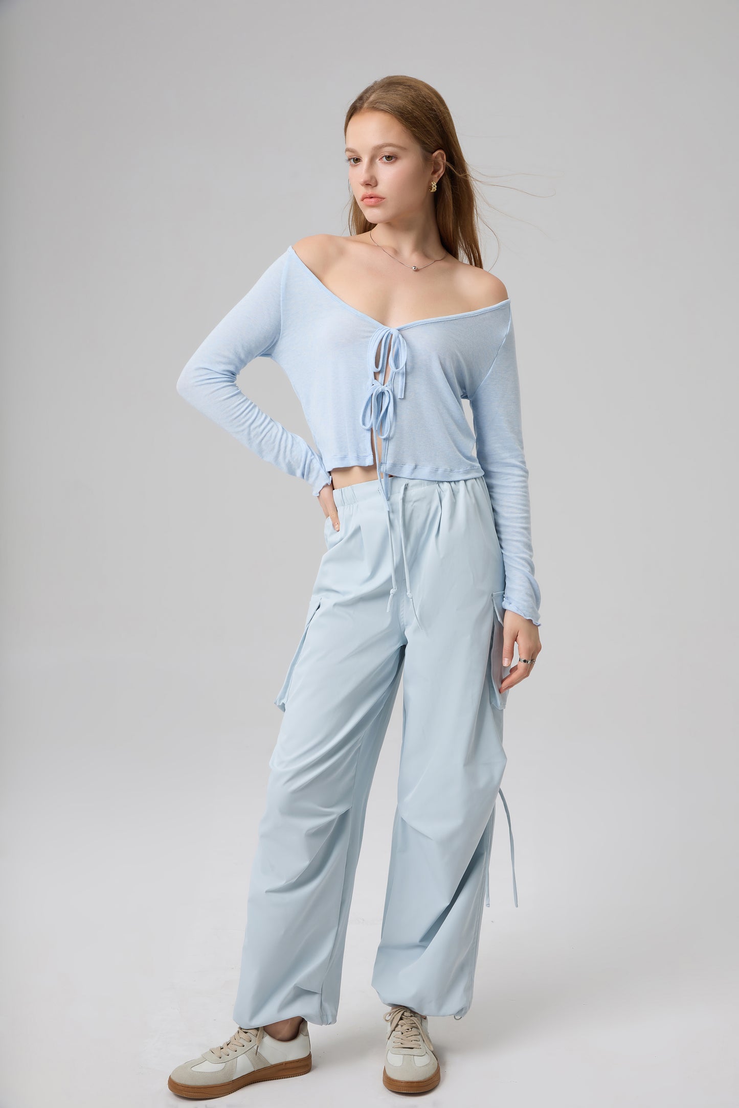 Woman wearing a light blue off-shoulder top and wide-leg pants on a gray background