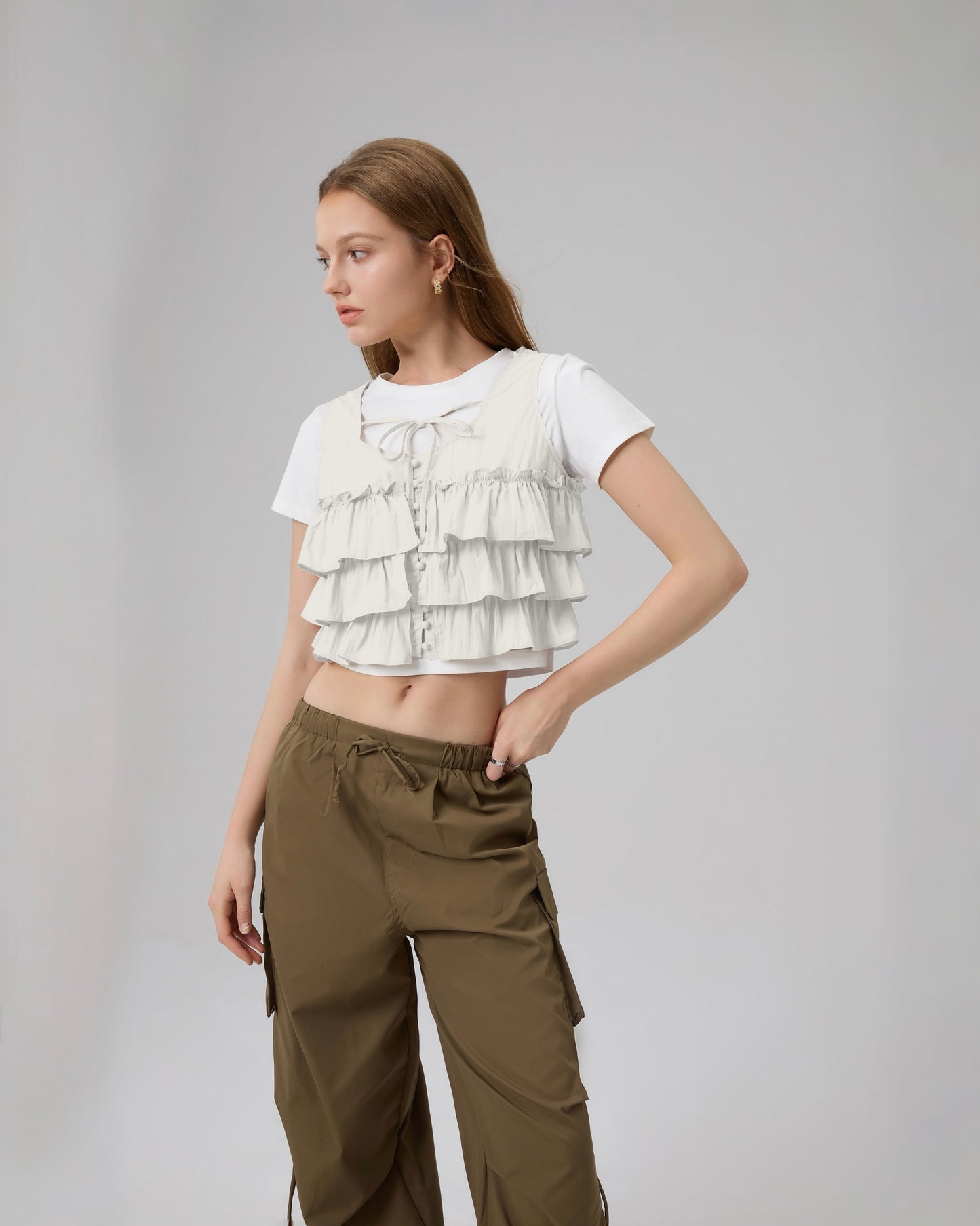 Woman wearing a white ruffled top and brown pants on a gray background