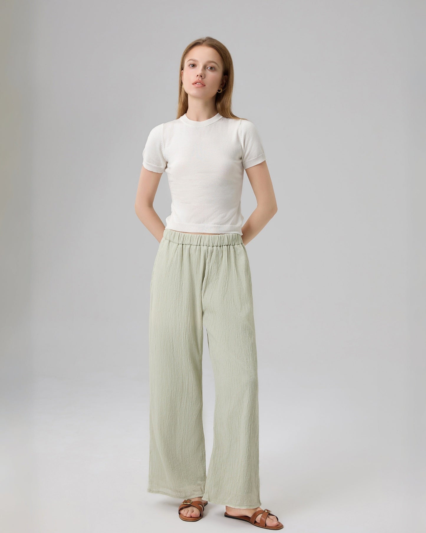 Woman wearing a white top and light green pants on a plain background