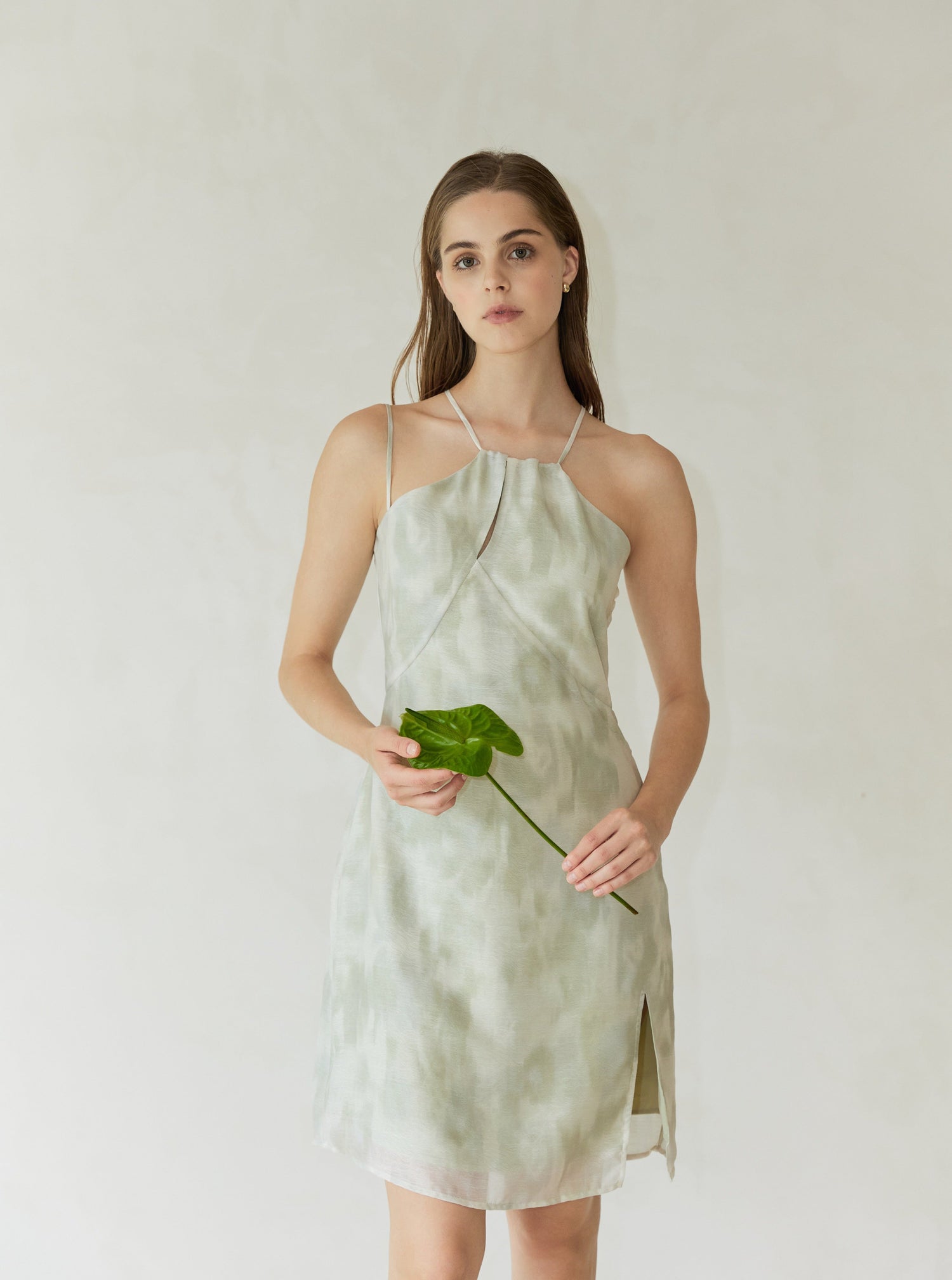 A model wearing a green, white, and gray halter dress with a floral pattern, featuring a side button closure and a slit at the hem.