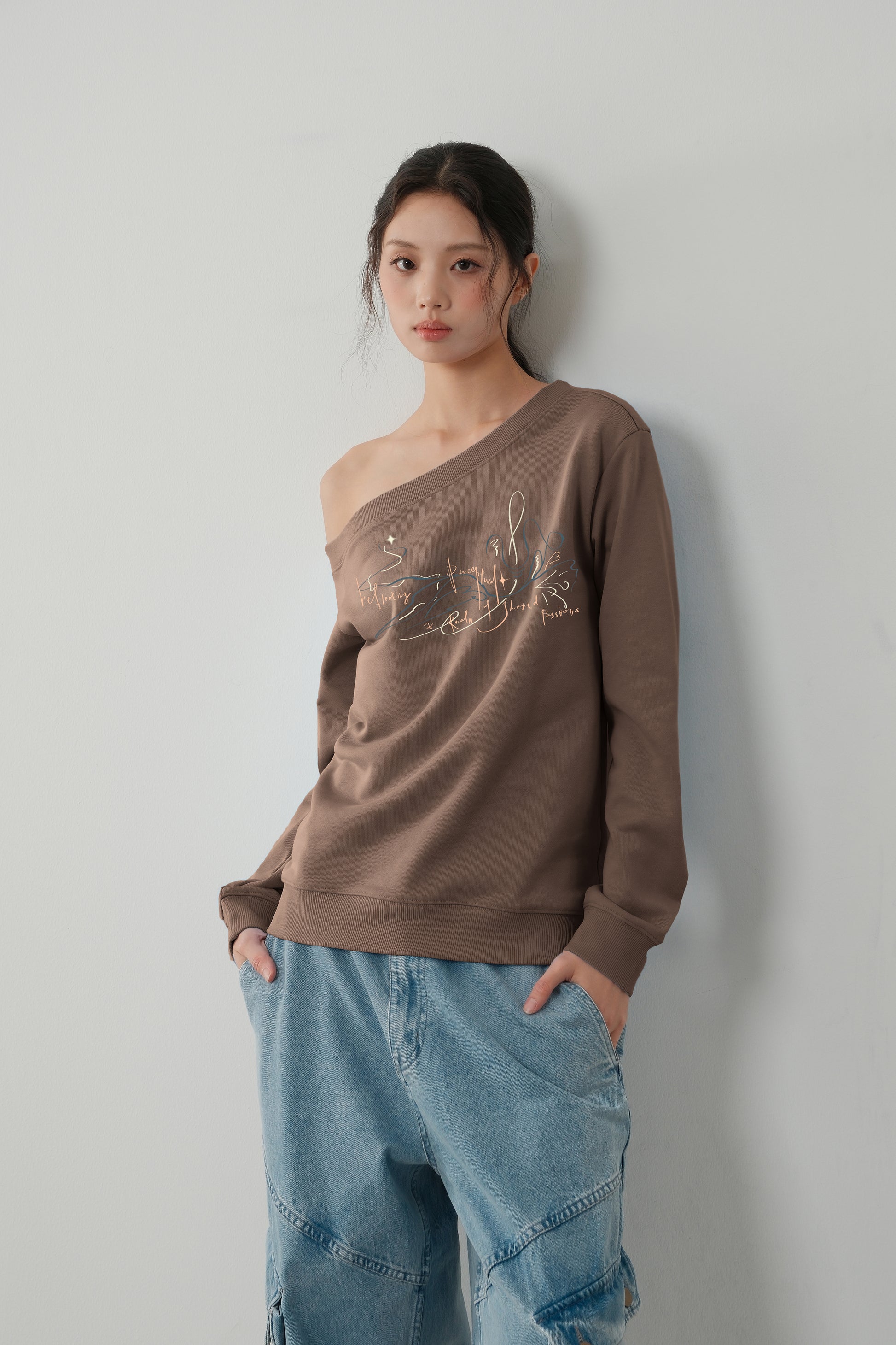 Model wearing The Lethe One Shoulder Sweatshirt in Cold Brew, asymmetric off-shoulder cotton-blend pullover front view.