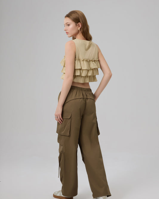 Woman wearing a layered beige top and green cargo pants on a light gray background