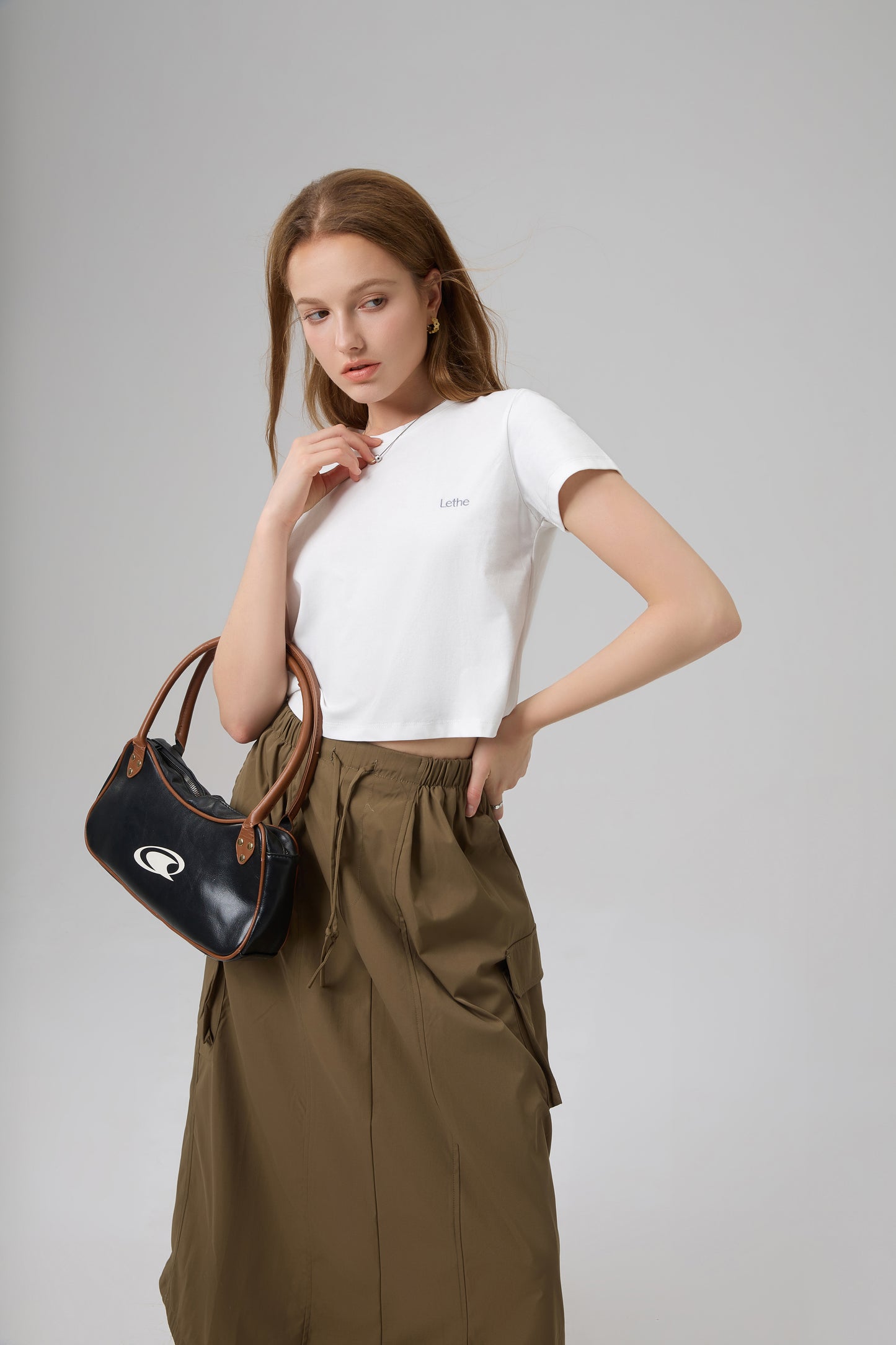 Model styling The Lethe Logo Tee in Star White with olive cargo skirt and black handbag, clean minimalist outfit.