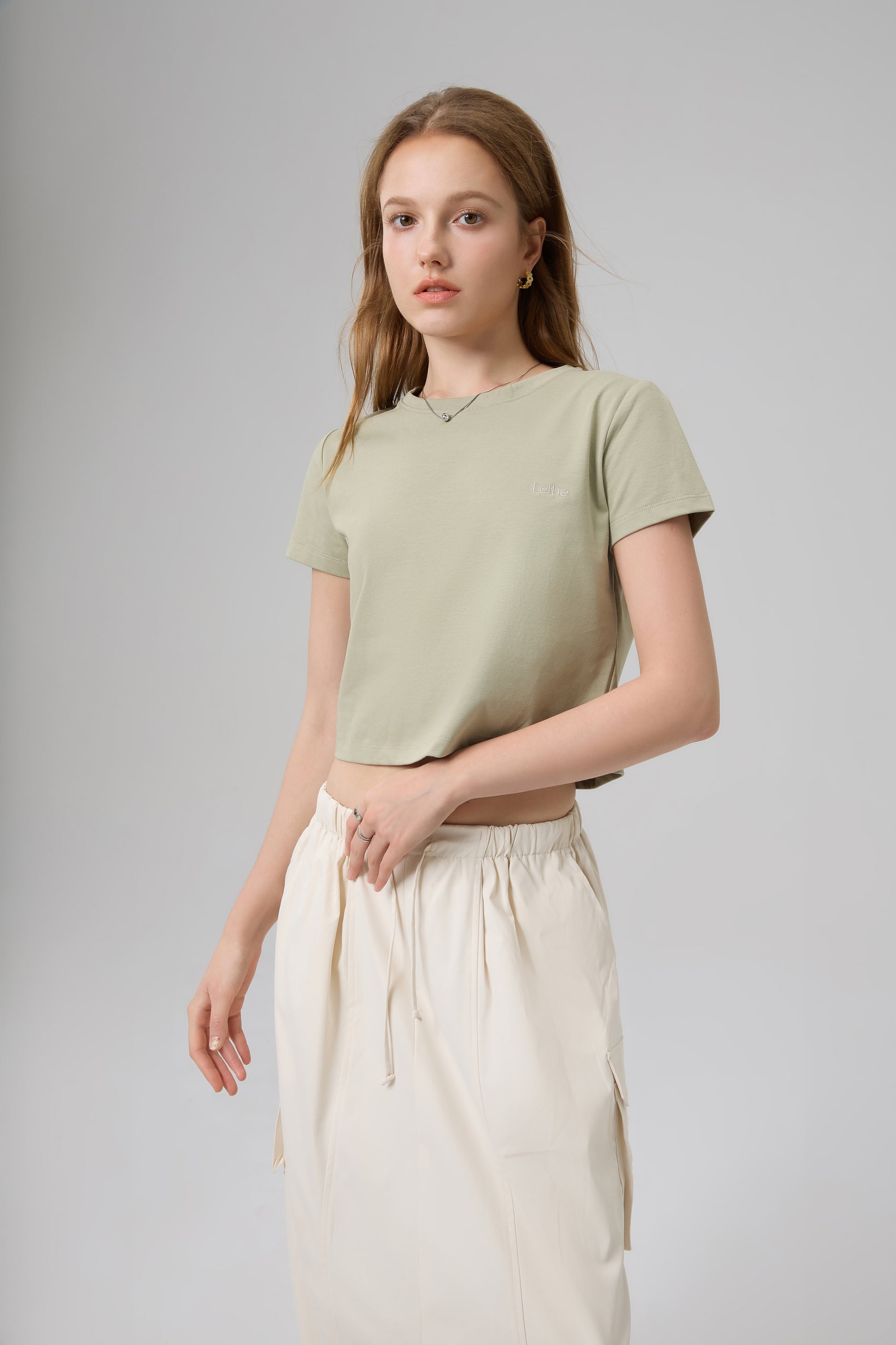Model wearing The Lethe Logo Tee in Desert Taupe paired with ivory skirt, minimalist cropped cotton t-shirt front view.