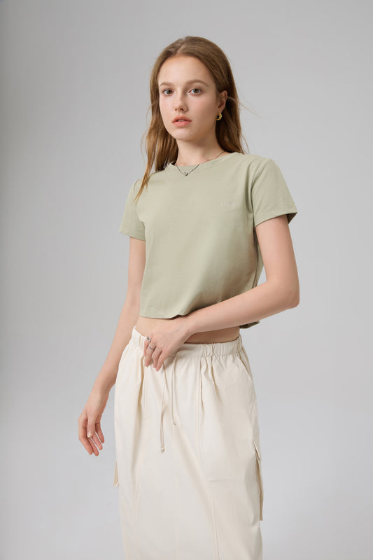Model wearing The Lethe Logo Tee in Desert Taupe paired with ivory skirt, minimalist cropped cotton t-shirt front view.