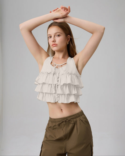 Woman wearing a layered ruffle top and brown pants against a plain background