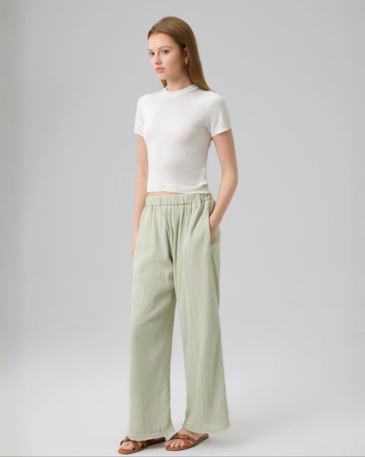 Woman wearing a white top and light green pants on a gray background