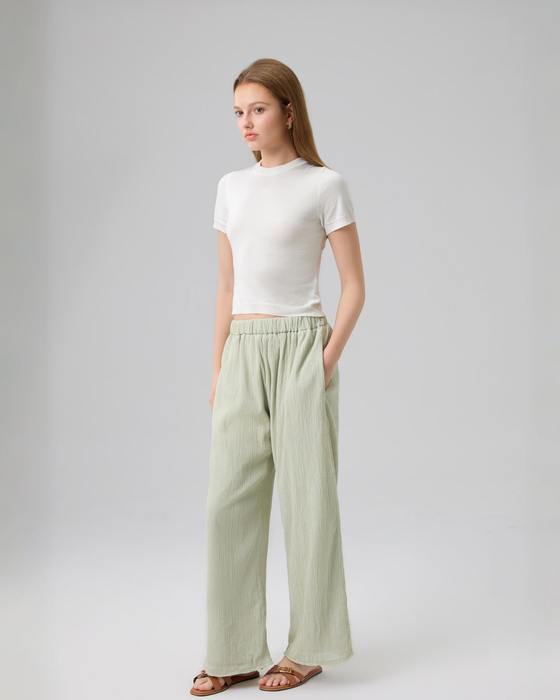 Woman wearing a white top and light green pants on a gray background