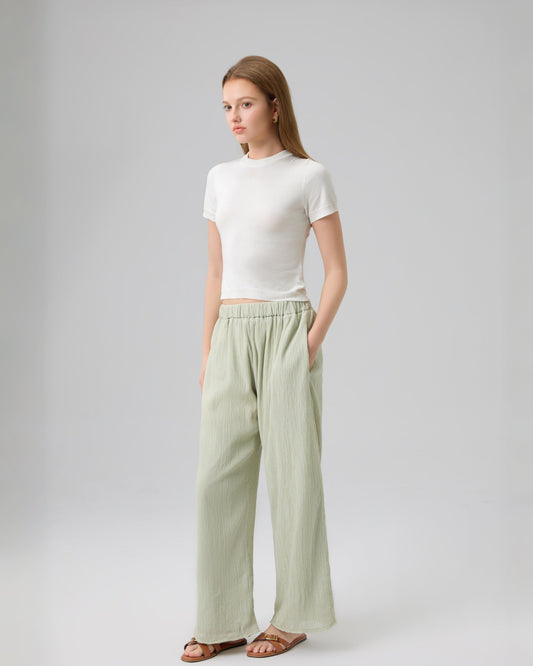 Woman wearing a white top and light green pants on a gray background